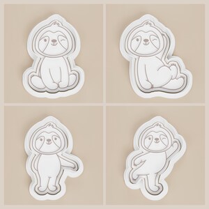 May include: Four white sloth-shaped cookie cutters in different poses. Each cutter has a detailed outline of a winking sloth with a rounded head and body. The cutters are on a light beige background.