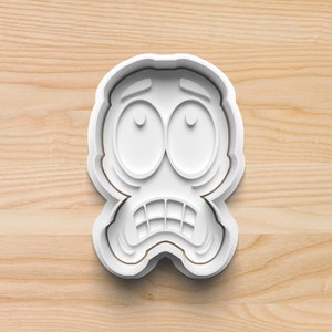 May include: White plastic cookie cutter shaped like a cartoon face with wide eyes and a worried expression.
