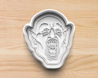 May include: White plastic cookie cutter shaped like a monster's face with a wide open mouth and sharp teeth.