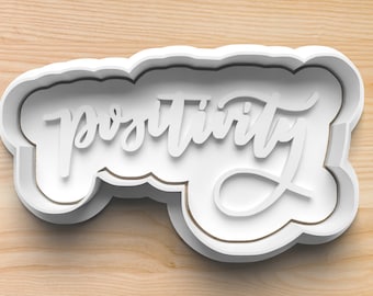 May include: White plastic cookie cutter shaped like the word "positivity" in a handwritten font.