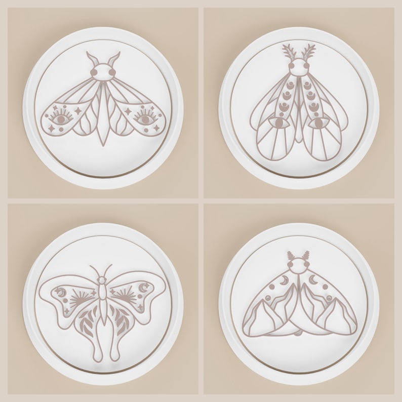 May include: Four white ceramic coasters with a gold rim, each featuring a different moth or butterfly design in shades of brown. The insect illustrations have intricate details, including eyes, moons, and suns.