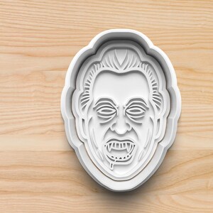 May include: White plastic cookie cutter shaped like a vampire's face with fangs and dripping blood.