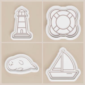 May include: Four white cookie cutters with brown outlines. The shapes include a lighthouse, a life preserver, a seal, and a sailboat. The cookie cutters are on a light beige background.