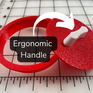 May include: A red plastic cookie cutter with an ergonomic handle. The cutter is in the shape of a heart. The text "Ergonomic Handle" is displayed on the image.