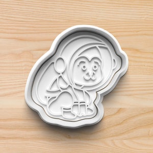 May include: White plastic cookie cutter shaped like a cartoon astronaut wearing a spacesuit.
