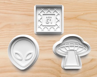 May include: Three white plastic cookie cutters shaped like an alien head, a UFO, and a square with the text "Area 51" inside.