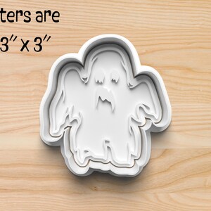 May include: White plastic cookie cutter shaped like a ghost with a toothy grin. Cutters are approximately 7.6 cm by 7.6 cm.