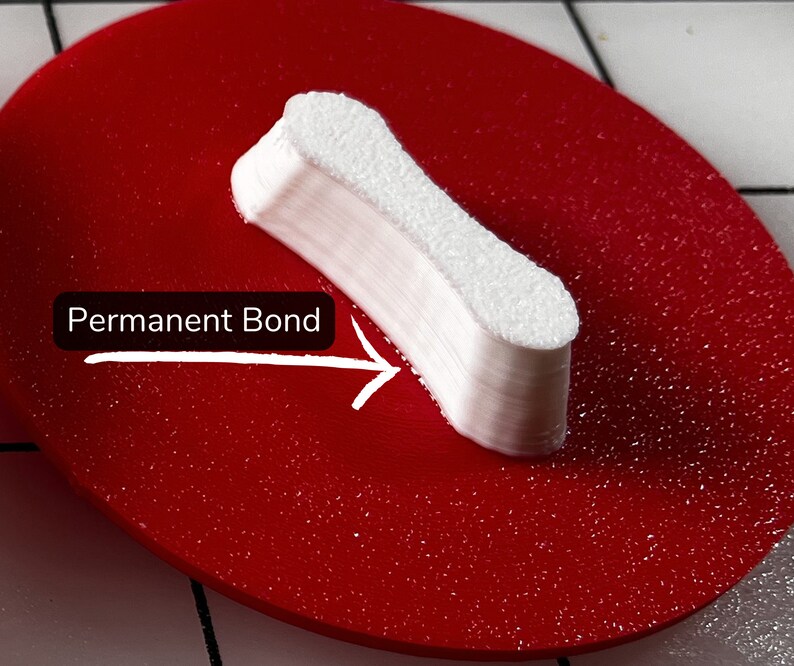 May include: A white, rectangular object with a textured surface, labeled "Permanent Bond" with an arrow, is placed on a red, circular surface. The object appears to be made of stacked layers, suggesting a bonding or adhesive product.