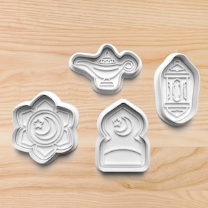 May include: Four white plastic cookie cutters shaped like a crescent moon and star, a mosque, a lantern, and a genie lamp.