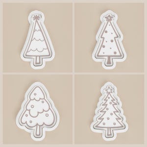 May include: Four white Christmas tree-shaped cookie cutters with brown outlines. Each cutter has a different design, including wavy lines, dots, and star accents. The cutters are set against a neutral background.