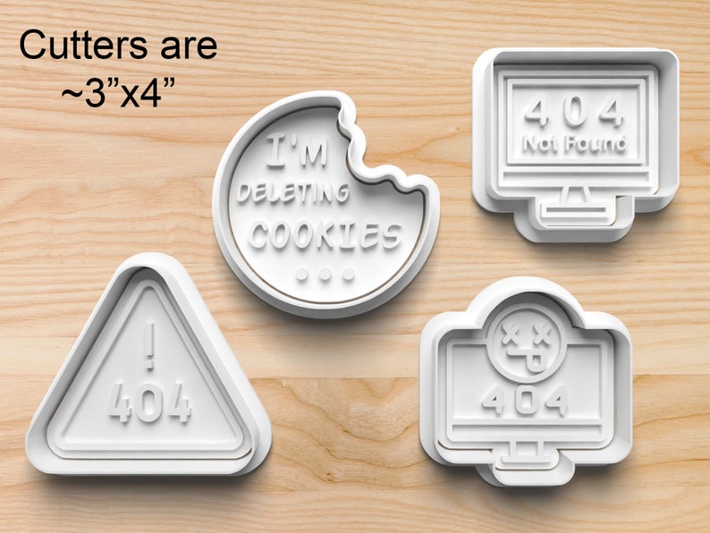 May include: Four white plastic cookie cutters shaped like a computer screen, a triangle with an exclamation point, a cookie with a bite taken out of it, and a computer screen with a face. The computer screens have the text "404 Not Found" and "404" on them. The triangle has the text "404" on it. The cookie has the text "I'M DELETING COOKIES" on it. The cutters are approximately 3 inches by 4 inches.