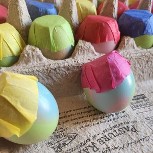 May include: A carton of eggs decorated with colorful tissue paper. The eggs are arranged in a carton with a brown paper background. The carton has text that reads "Pasture Raised" and "No Hormones No Antibiotics".