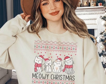 May include: Cream-colored sweatshirt with a festive design featuring four cartoon cats wearing Santa hats and scarves. The text "MEOWY CHRISTMAS" is below the cats. The sweatshirt has a fair isle pattern in red and green.