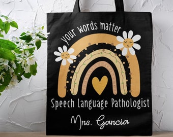 May include: Black tote bag with a rainbow design and the text "Your words matter" and "Speech Language Pathologist Mrs. Garcia".
