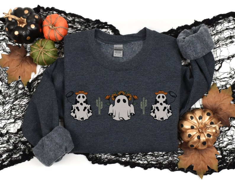 May include: A dark gray sweatshirt with a graphic of three ghosts wearing cowboy hats and holding lassoes. The ghosts are surrounded by cacti and sunflowers.