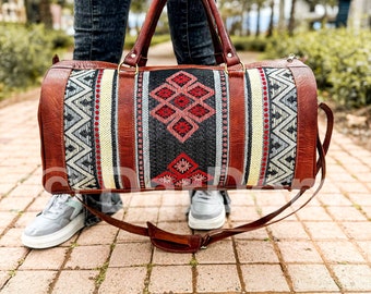 Puede incluir: Una bolsa de viaje de cuero marrón con un patrón tejido colorido. La bolsa tiene una correa larga y un asa superior.