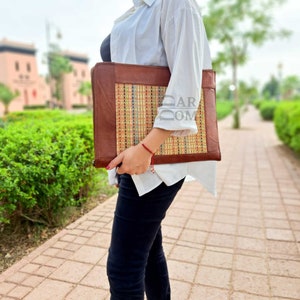 May include: A brown leather laptop case with a woven straw insert. The case has a flap closure and a handle.