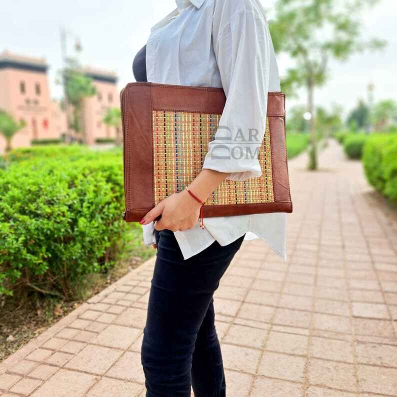 May include: A brown leather laptop case with a woven straw insert. The case has a flap closure and a handle.