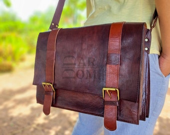 May include: A dark brown leather messenger bag with a flap closure, two brown leather straps, and gold-colored buckles. The bag has a shoulder strap and is worn across the body. The bag has the text "DAR DOM" embossed on the front.