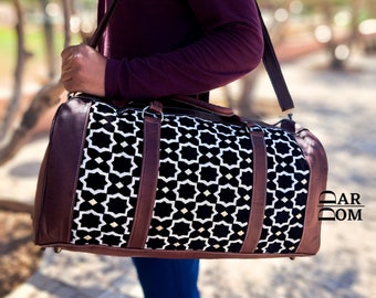 Puede incluir: Una bolsa de lona con estampado geométrico en blanco y negro con detalles en cuero marrón. La bolsa tiene una correa para el hombro y un asa superior. La bolsa se lleva sobre el hombro de una persona.