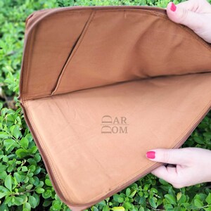 May include: A brown laptop sleeve with a zipper closure. The inside of the sleeve is lined with a brown fabric. The sleeve has a logo that says "DAR DOM" on the inside.