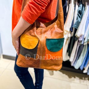 May include: A brown leather shoulder bag with colorful patchwork pockets. The pockets are orange, black, green, and red.