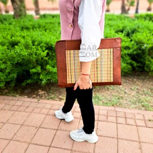 May include: A brown leather laptop case with a woven straw insert. The case has a flap closure and a handle.
