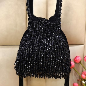 May include: A black beaded handbag with a drawstring closure and long tassels. The bag is made of black velvet and is decorated with black beads.