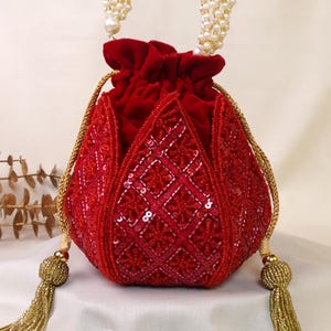 Puede incluir: Un bolso de terciopelo rojo con cordón y detalles de lentejuelas en forma de rombos. Cuenta con un asa de perlas y borlas doradas. Un accesorio elegante para ocasiones especiales.