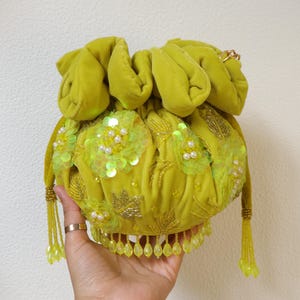 Puede incluir: Un bolso tipo saco de terciopelo color chartreuse con cierre de cordón, decorado con motivos florales de lentejuelas, cuentas y perlas. Incluye un fleco de cuentas en el borde inferior y dos borlas laterales con cuentas doradas, con un cierre fruncido.