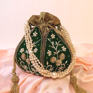 Könnte beinhalten: Ein smaragdgrüner Beutel mit goldener Stickerei und Perlenbesatz. Der Beutel hat einen perlenbesetzten Riemen und goldene Quasten. Er liegt auf einem rosa Satinhintergrund, der sein aufwendiges Design hervorhebt.