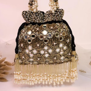May include: An ornate gold and black beaded handbag with mirror details and pearl fringe. The bag has a drawstring closure and beaded handles. The design features floral patterns and a luxurious aesthetic.