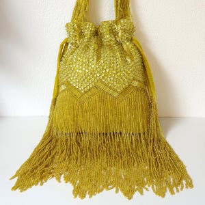 May include: A chartreuse drawstring handbag featuring intricate beadwork, sequins, and a chevron pattern. The bag includes a single handle and a long, dense fringe of matching beads hanging from the base, creating a textured, monochromatic appearance.