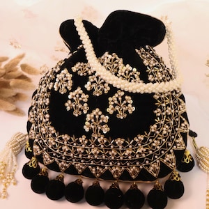 Op de afbeelding: Zwarte fluwelen buideltas met ingewikkelde gouden en parel borduursels. De tas heeft een trekkoordsluiting, zwarte pompom franjes en een parel kralen handvat. Een luxe accessoire voor speciale gelegenheden.