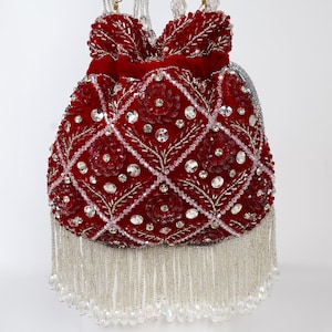 Puede incluir: Un bolso de mano de terciopelo rojo con intrincados patrones de diamantes, adornado con brillantes pedrería y detalles florales. El bolso presenta flecos de cuentas y correas de cuentas, creando un accesorio elegante.
