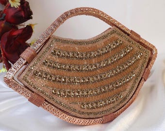May include: A rose gold beaded clutch with a decorative metal frame and a top handle. The clutch is embellished with gold beads and sequins.