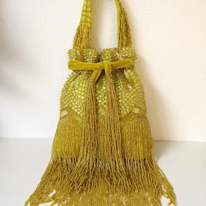 May include: A chartreuse drawstring handbag featuring an intricate exterior of glass beads and sequins in geometric patterns. The bag includes a matching velvet ribbon tie closure and a long, dense fringe of hanging beads at the bottom edge.