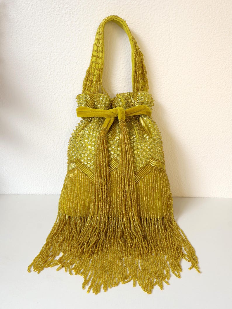 May include: A chartreuse drawstring handbag featuring an intricate exterior of glass beads and sequins in geometric patterns. The bag includes a matching velvet ribbon tie closure and a long, dense fringe of hanging beads at the bottom edge.