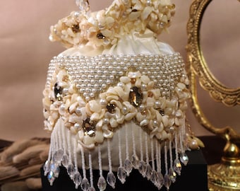 Puede incluir: Un bolso blanco de cordón con cuentas con un adorno de perlas y cristales. El bolso tiene una larga franja de cuentas.