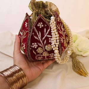 May include: A red velvet pouch with gold embroidery and pearl accents. The pouch has a drawstring closure and a long pearl chain with a gold tassel.