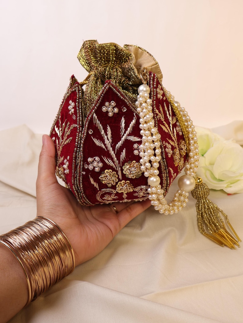 May include: A red velvet pouch with gold embroidery and pearl accents. The pouch has a drawstring closure and a long pearl chain with a gold tassel.