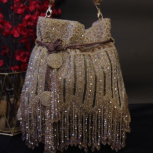 May include: A gold beaded handbag with a drawstring closure and a shoulder strap. The bag features intricate beadwork, a decorative knot, and dangling crystal fringe. The bag is a stylish accessory for special occasions.