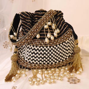 Puede incluir: Bolso negro con cordón y cuentas con detalles dorados y blancos. El bolso presenta una correa de terciopelo negro, ribete de cuentas doradas y cuentas colgantes con forma de perla. Borlas doradas cuelgan de la parte inferior, añadiendo un toque de elegancia.