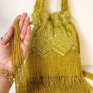 May include: A chartreuse drawstring handbag featuring intricate beadwork and sequins in a chevron pattern. The bag includes a beaded handle and long, dangling beaded fringe along the bottom edge. The drawstring closure is accented with beaded tassels.