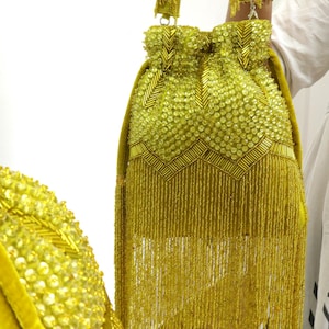 May include: A lime green drawstring handbag featuring extensive beadwork and sequin embellishments in a chevron pattern. The bag includes a matching beaded handle and a long, dense fringe of hanging beads extending from the base of the main body.