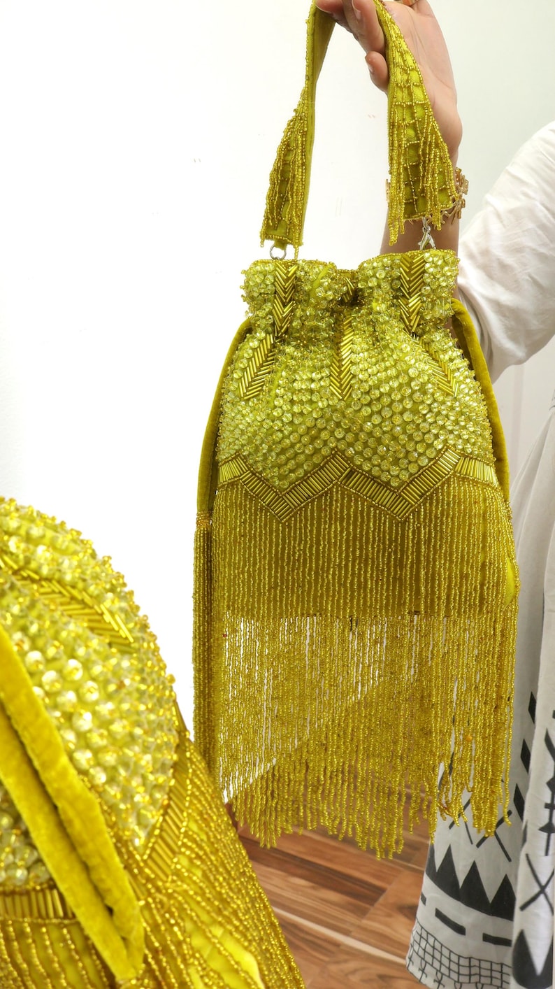 May include: A lime green drawstring handbag featuring extensive beadwork and sequin embellishments in a chevron pattern. The bag includes a matching beaded handle and a long, dense fringe of hanging beads extending from the base of the main body.