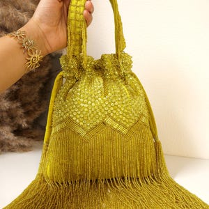 May include: A chartreuse drawstring handbag featuring an intricate exterior of glass beads and sequins. The bag displays a chevron pattern of baguette beads, a top handle with beaded lattice detailing, and a long fringe of dangling beads.