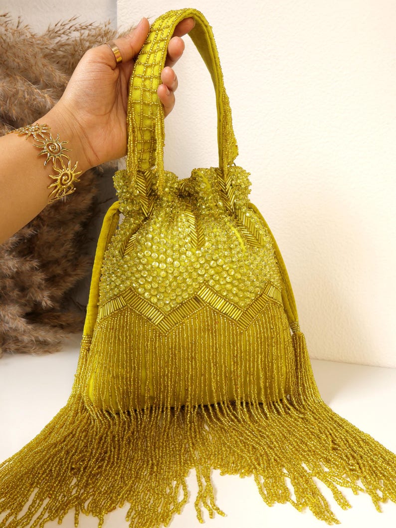 May include: A chartreuse drawstring handbag featuring an intricate exterior of glass beads and sequins. The bag displays a chevron pattern of baguette beads, a top handle with beaded lattice detailing, and a long fringe of dangling beads.