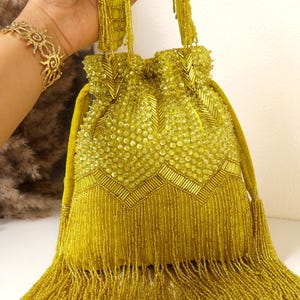 May include: A chartreuse drawstring handbag featuring an intricate exterior of glass beads and sequins. The bag is adorned with a chevron pattern of bugle beads and a dense fringe of long, dangling beads at the base. It includes a matching beaded handle.