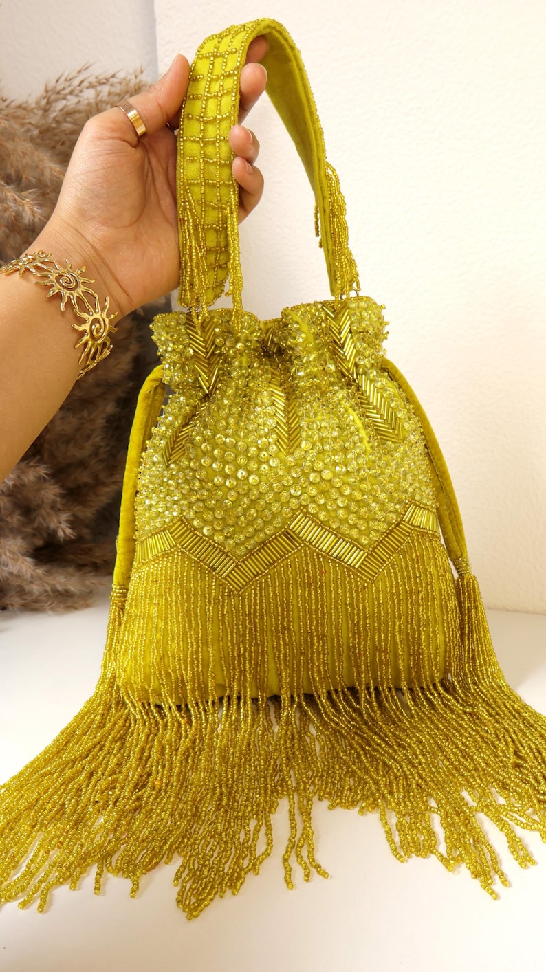 May include: A chartreuse drawstring handbag featuring an intricate exterior of glass beads and sequins. The bag is adorned with a chevron pattern of bugle beads and a dense fringe of long, dangling beads at the base. It includes a matching beaded handle.